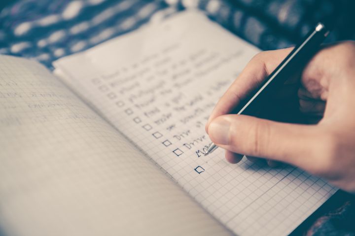 Person's hand holding a pen adding entries to a notepad todo list