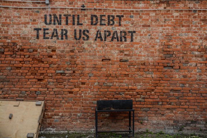 A wall with the words "until debt tear us apart" stenciled on the bricks