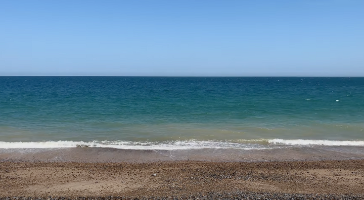 picture of shingle beach, small wave hitting the beach with sea and sky in the distance