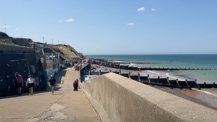 Foreground view of concrete sea front, background view of beach and sea and low cliffs in the distance